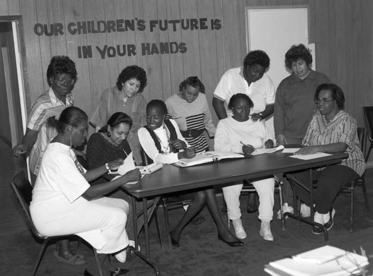 Head Start parents at the Urban League Head Start in Los Angeles gather around a table to plan in 1991 under a banner that says "Our Children's Future is in your Hands."