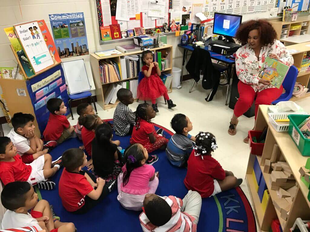 An adult woman reads to grade school aged children in a classroom setting